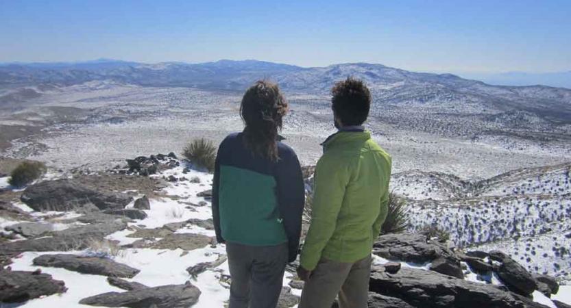 Two people face away from the camera, looking out over a vast snowy landscape. 